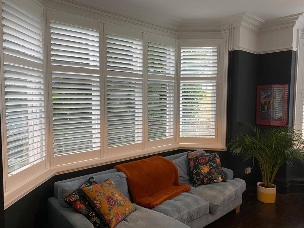 Finished shutters fitted in a bay window above a sofa